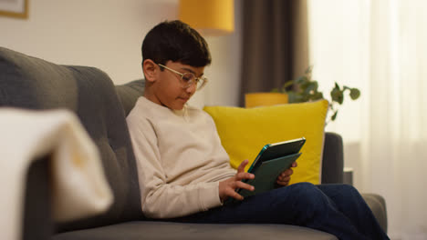 Kleiner-Junge-Sitzt-Zu-Hause-Auf-Dem-Sofa-Und-Spielt-Spiele-Oder-Streamt-Inhalte-Auf-Ein-Digitales-Tablet-1